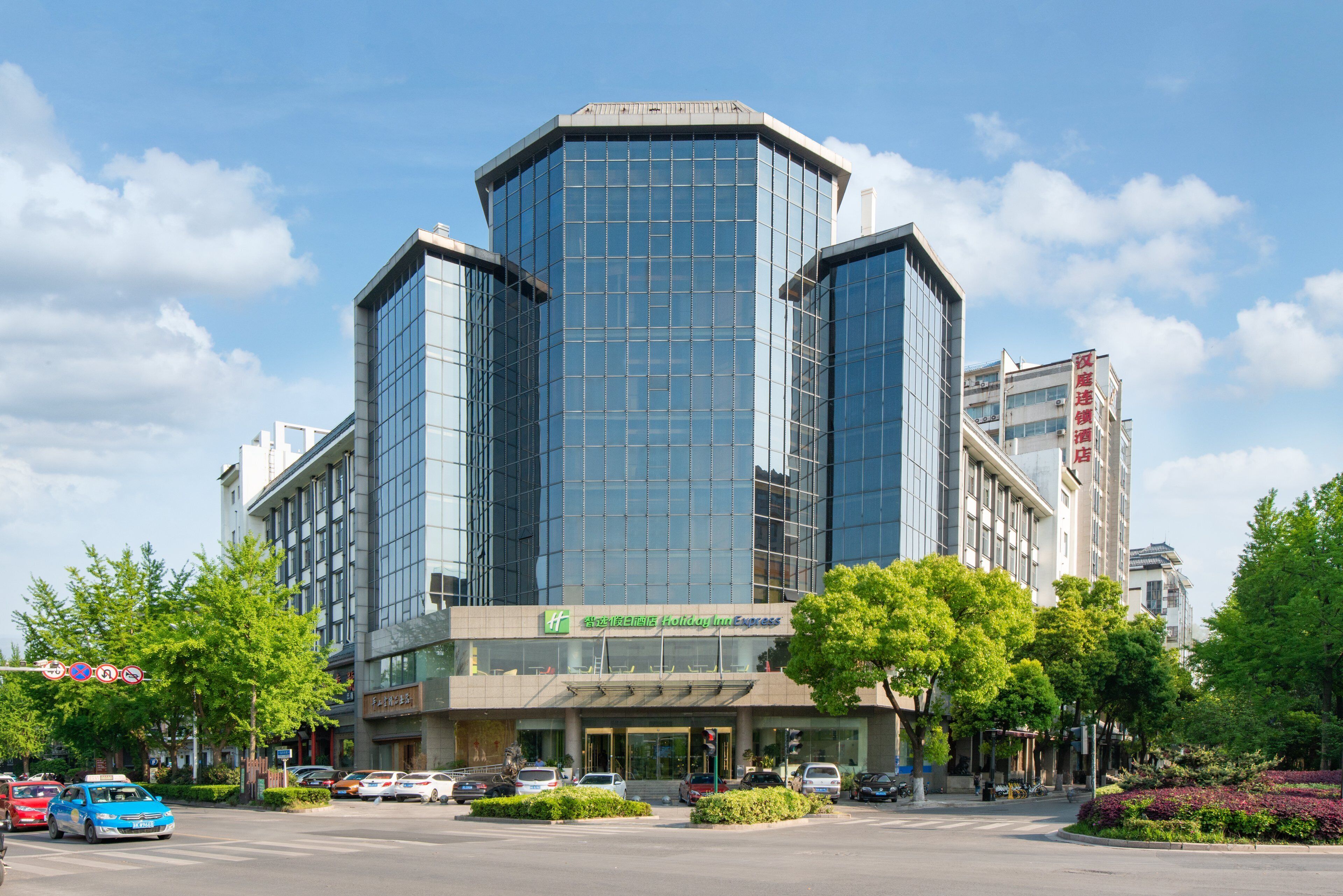 A modern hotel with a glass facade, a Holiday Inn Express sign, and a parking lot with several cars.