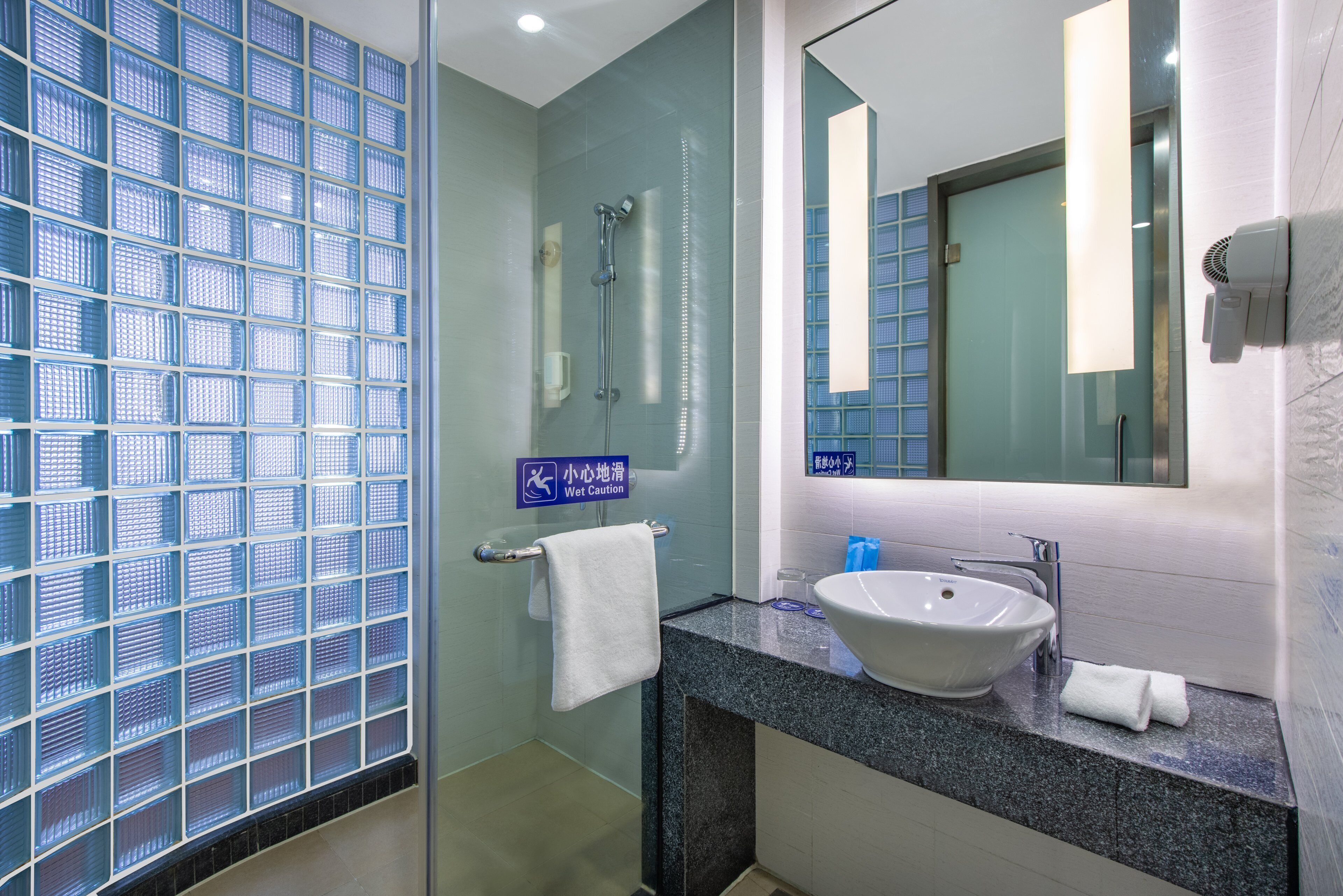 Un baño moderno con cabina de ducha de vidrio, un lavamanos con espejo y un perchero para toallas.