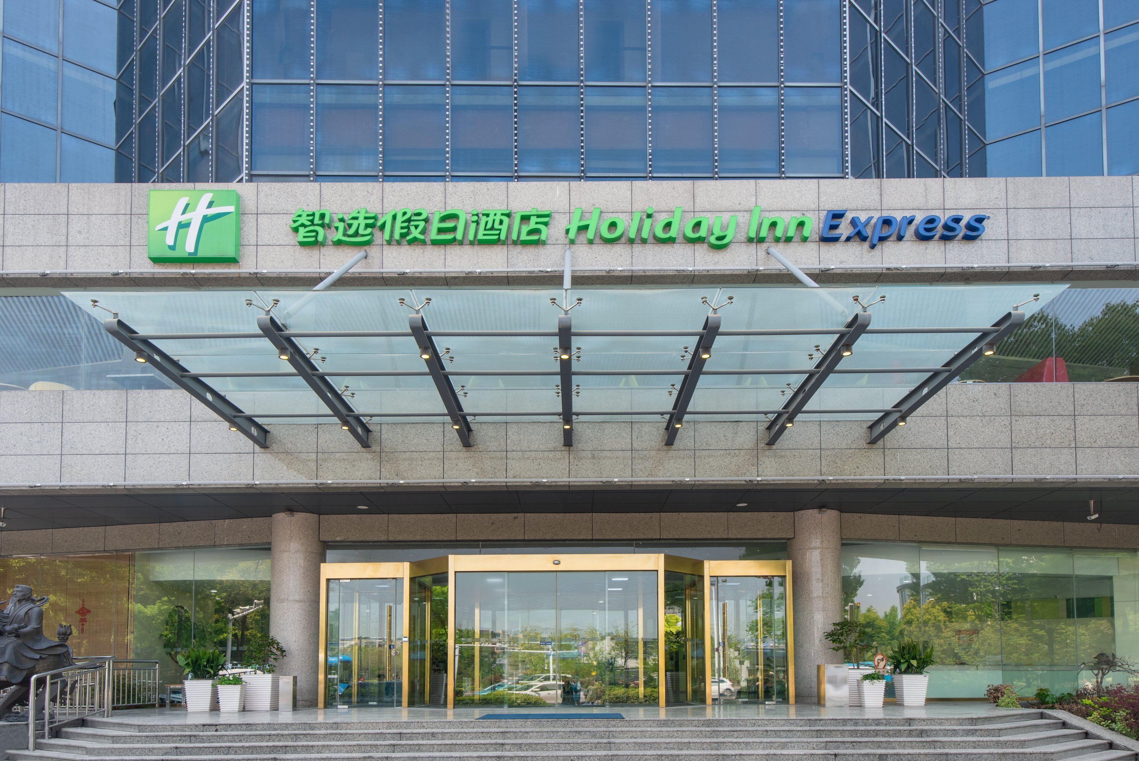 Der Eingang eines Holiday Inn Express Hotels mit einer Glaskuppel, großen Fenstern und einer Statue davor.