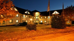 Een hotel met een centrale ingang, meerdere ramen en een vlaggenmast.