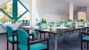 Een vergaderruimte met blauwgroene stoelen, een lange tafel en potplanten.
