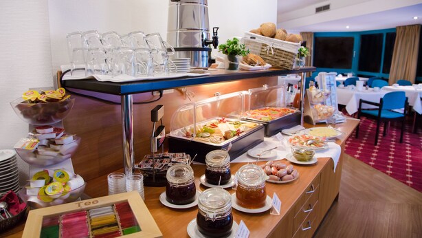 Een buffet met diverse etenswaren, waaronder potten jam, een koffiehoek en een keuze aan broden en gebak.