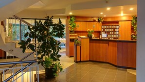 Een hotel lobby met een receptiebalie, houten kasten, kamerplanten en een trap.