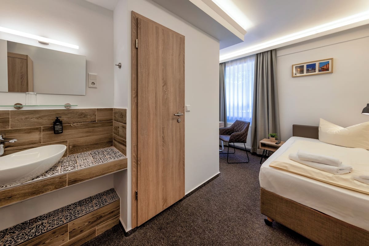 A hotel room with a wooden vanity, a large bed, a chair, and a view of the city through the window.