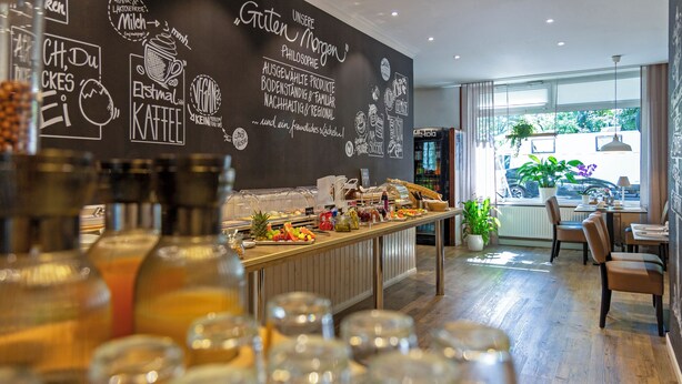 A cafe with a chalkboard wall displaying menu items and a counter with various food and drink options. - Auto-Parkhotel (Hamburg)