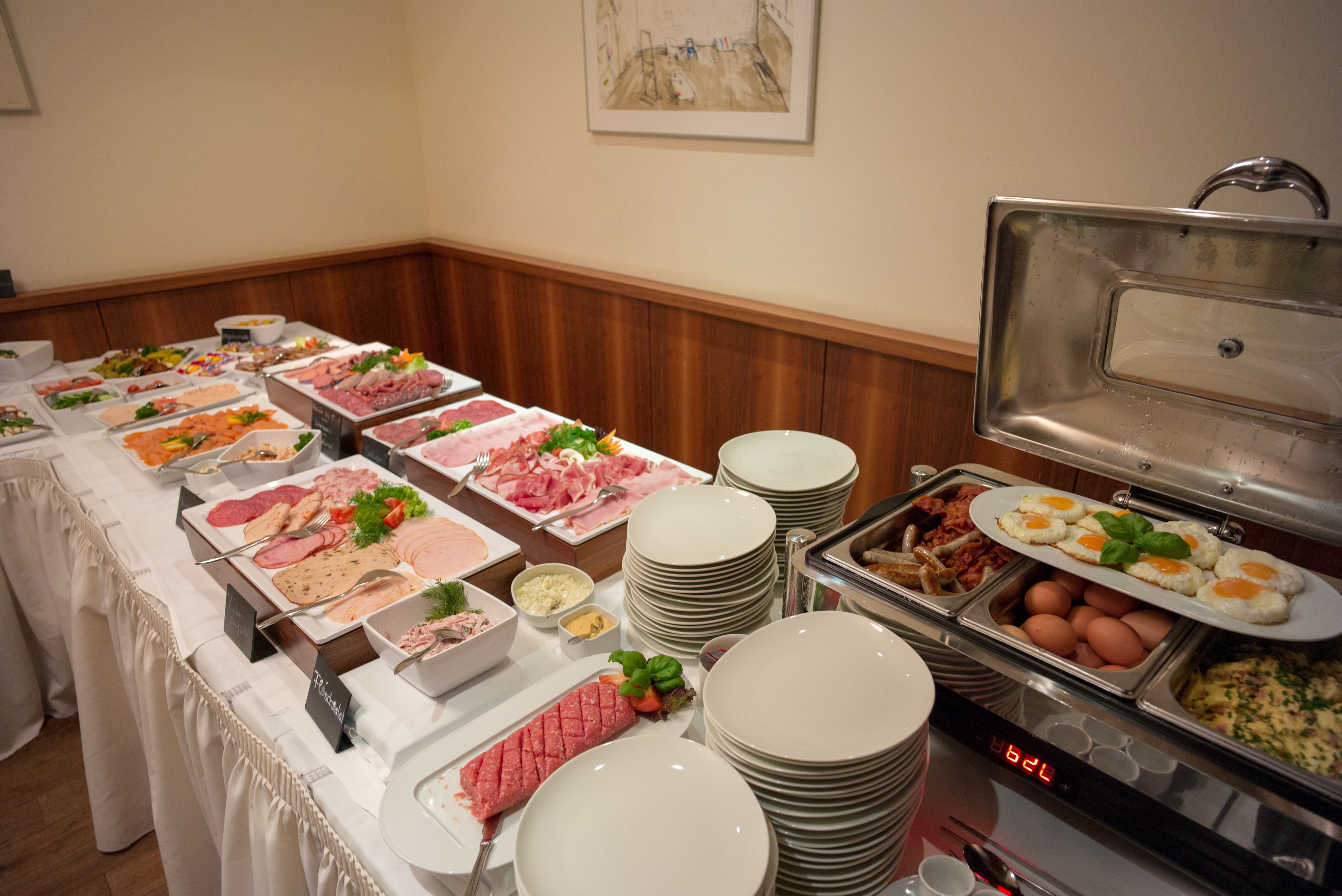 A buffet with various food items and a stack of white plates.