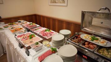 A buffet with various food items and a stack of white plates.