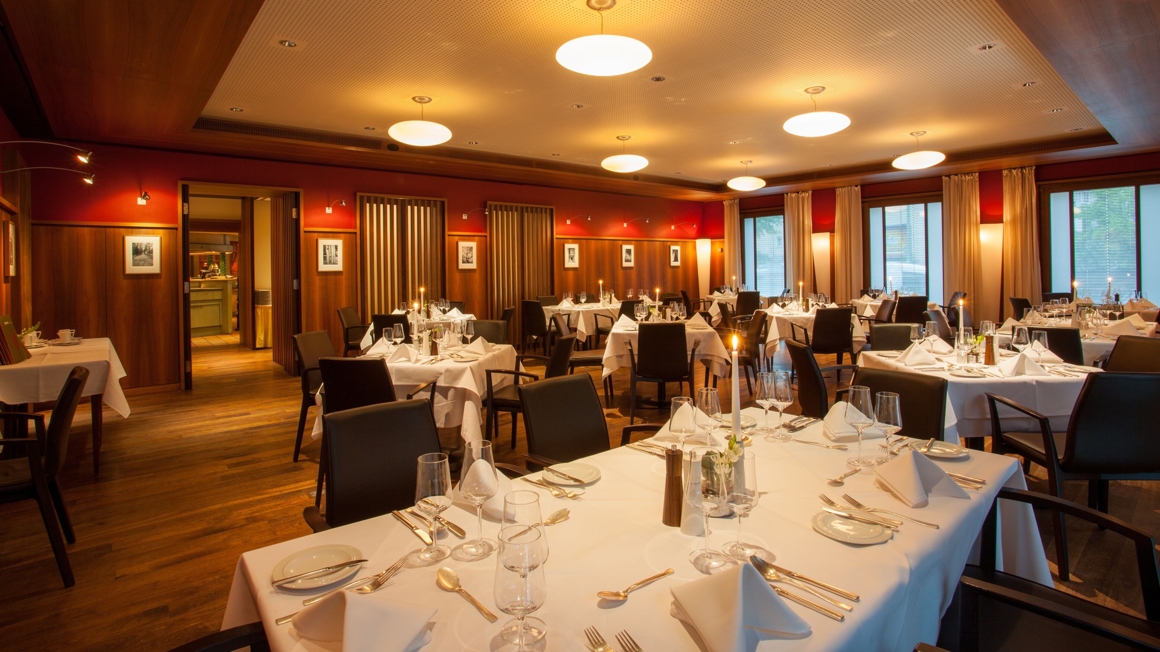 A restaurant with multiple tables set for dining, featuring white tablecloths and candles.