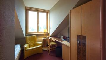 Una habitación pequeña y triangular con una cama, un sillón amarillo, un escritorio y un guardarropa.