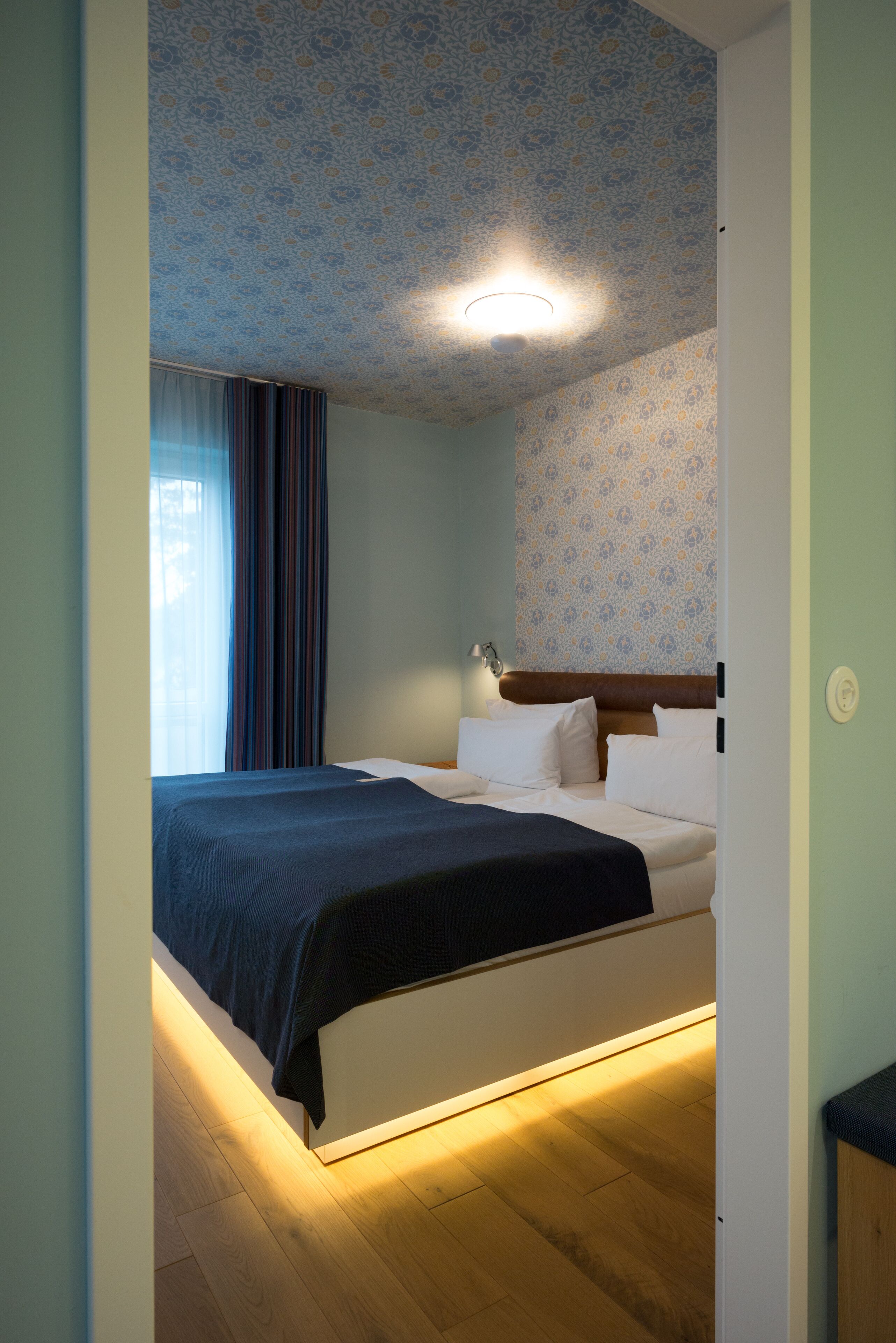 Un dormitorio con una cama, un mesita de noche, una lámpara y una ventana con cortinas.