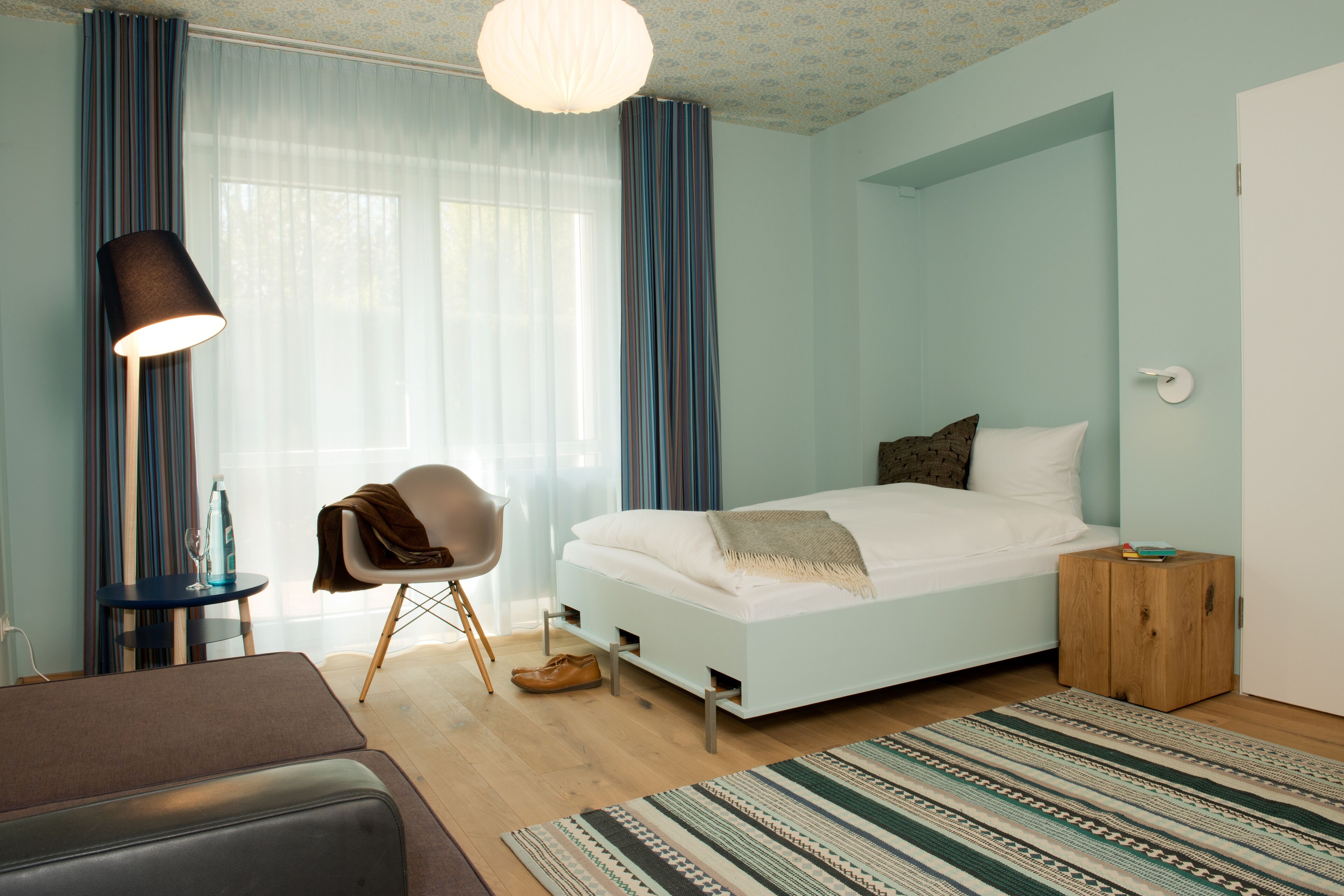 Een moderne slaapkamer met een bed, een stoel, een nachtkastje en een lamp.