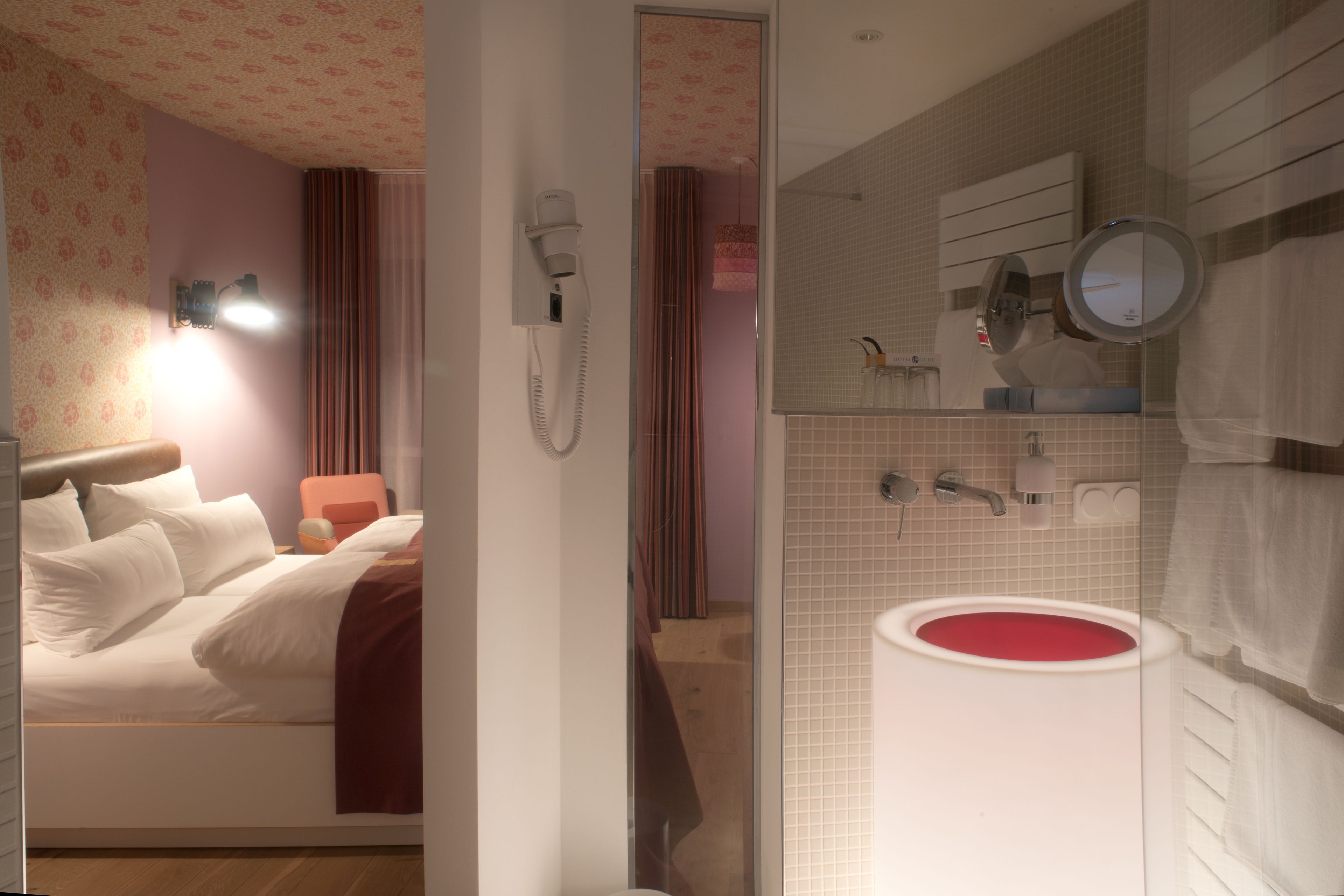 Una habitación de hotel con cama, baño con un lavamanos rojo y zona de ducha.