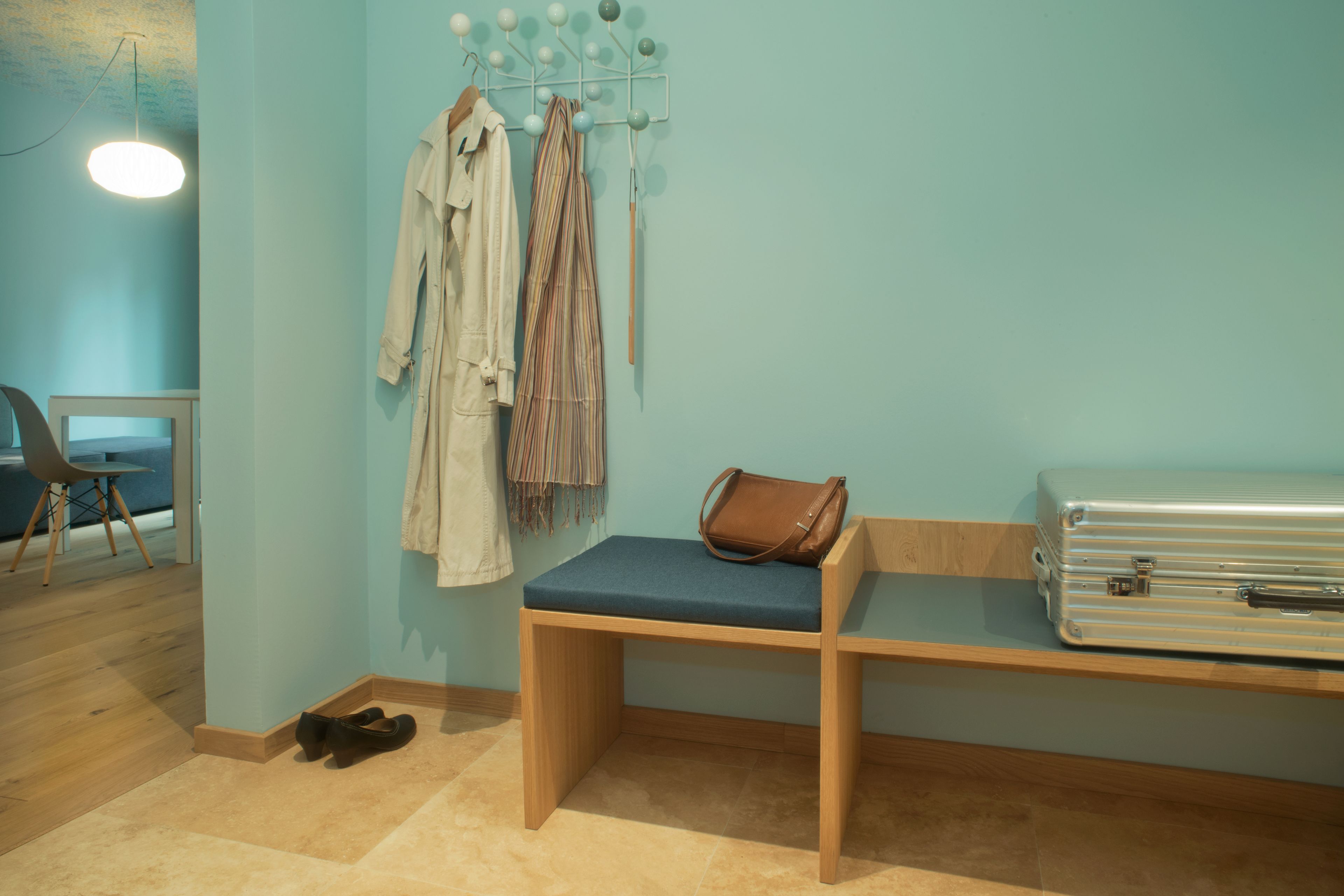 Une pièce avec un banc, un porte-manteau sur lequel sont suspendus des vêtements, une valise et une paire de chaussures posées sur le sol.