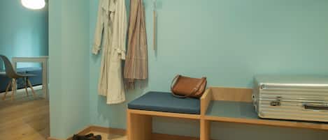 Una habitación con un banco, un perchero con ropa colgada, una maleta y un par de zapatos en el suelo.