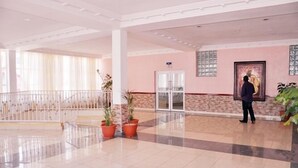 A spacious lobby with a tiled floor, a glass elevator, and potted plants. - Hotel Monte Carlo (Enugu)
