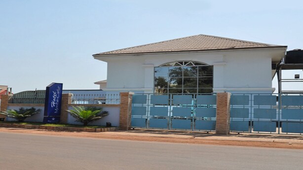 A two-story building with a gated entrance, a clear sky, and a road in the foreground. - Hotel Monte Carlo (Enugu)