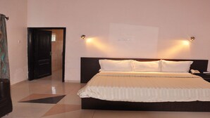 A hotel room with a large bed, two bedside tables, a nightstand, and a wall-mounted light fixture. - Hotel Monte Carlo (Enugu)