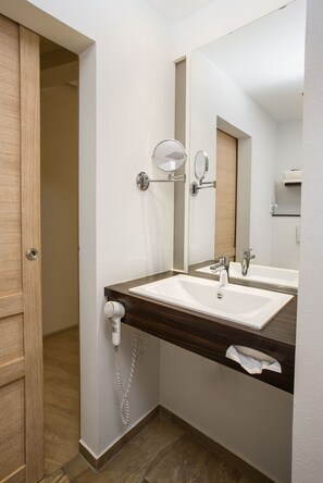Un baño con puerta de madera, un lavabo blanco, un espejo y un secador de pelo.