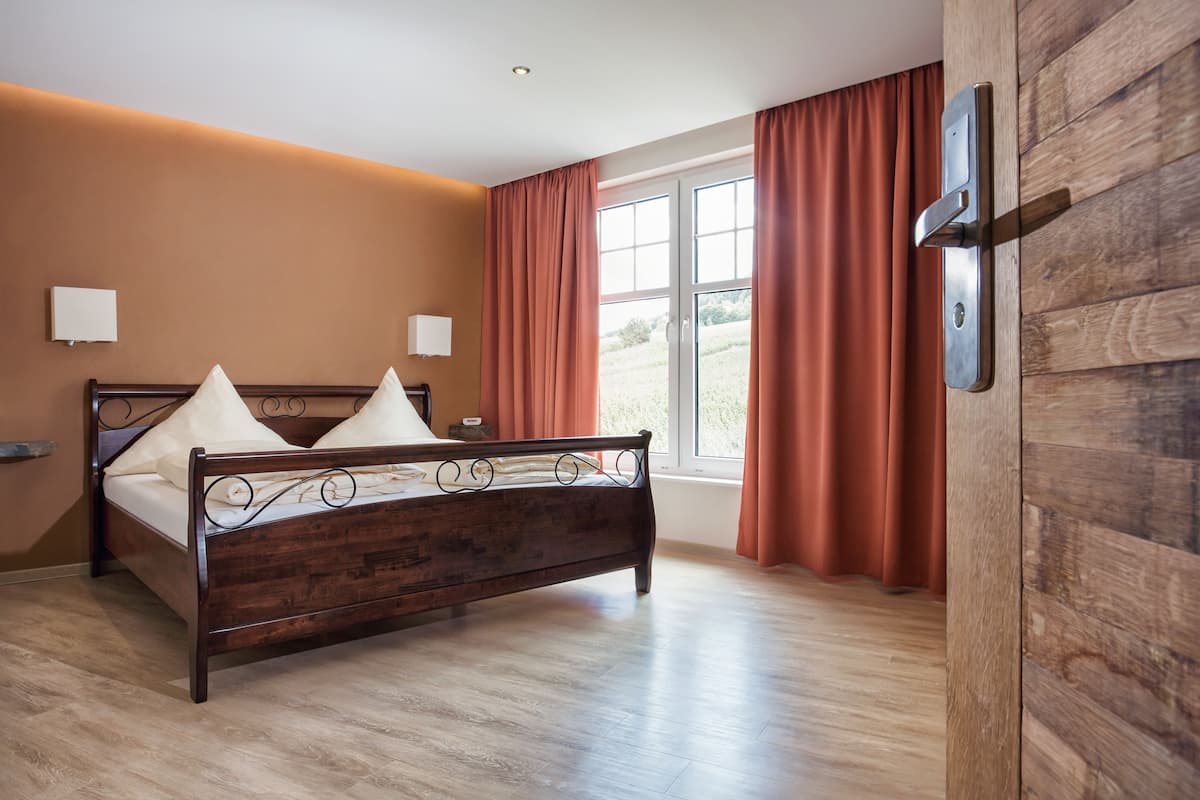 A bedroom with a wooden bed, two bedside tables, a window with curtains, and a wall-mounted light fixture.
