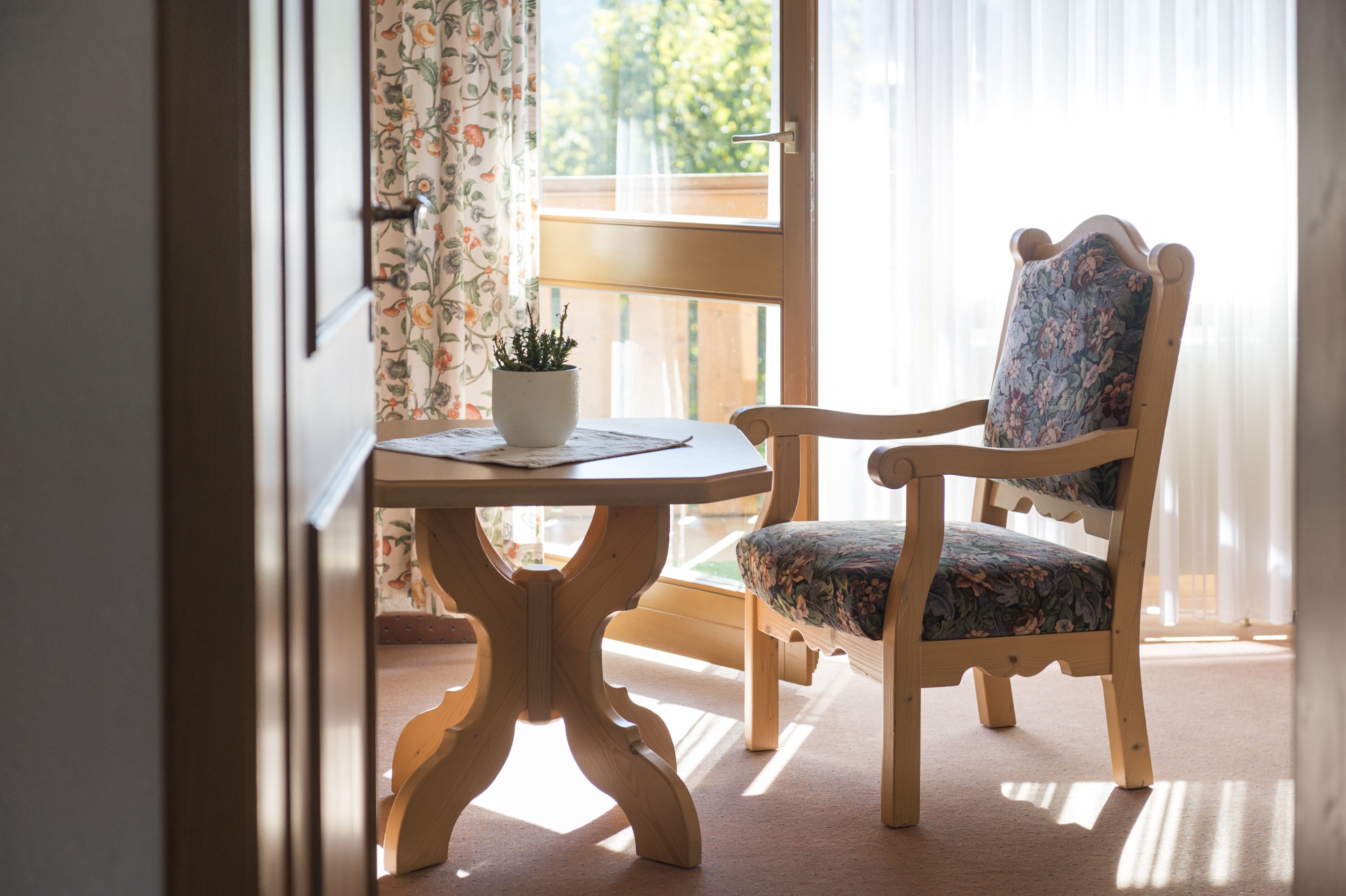 A wooden chair with floral upholstery and a small table with a potted plant.