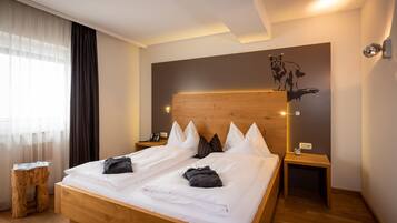 A hotel room with a wooden bed, white bedding, a wooden headboard, a wall-mounted artwork, a bedside table with a lamp, and a small wooden stool.