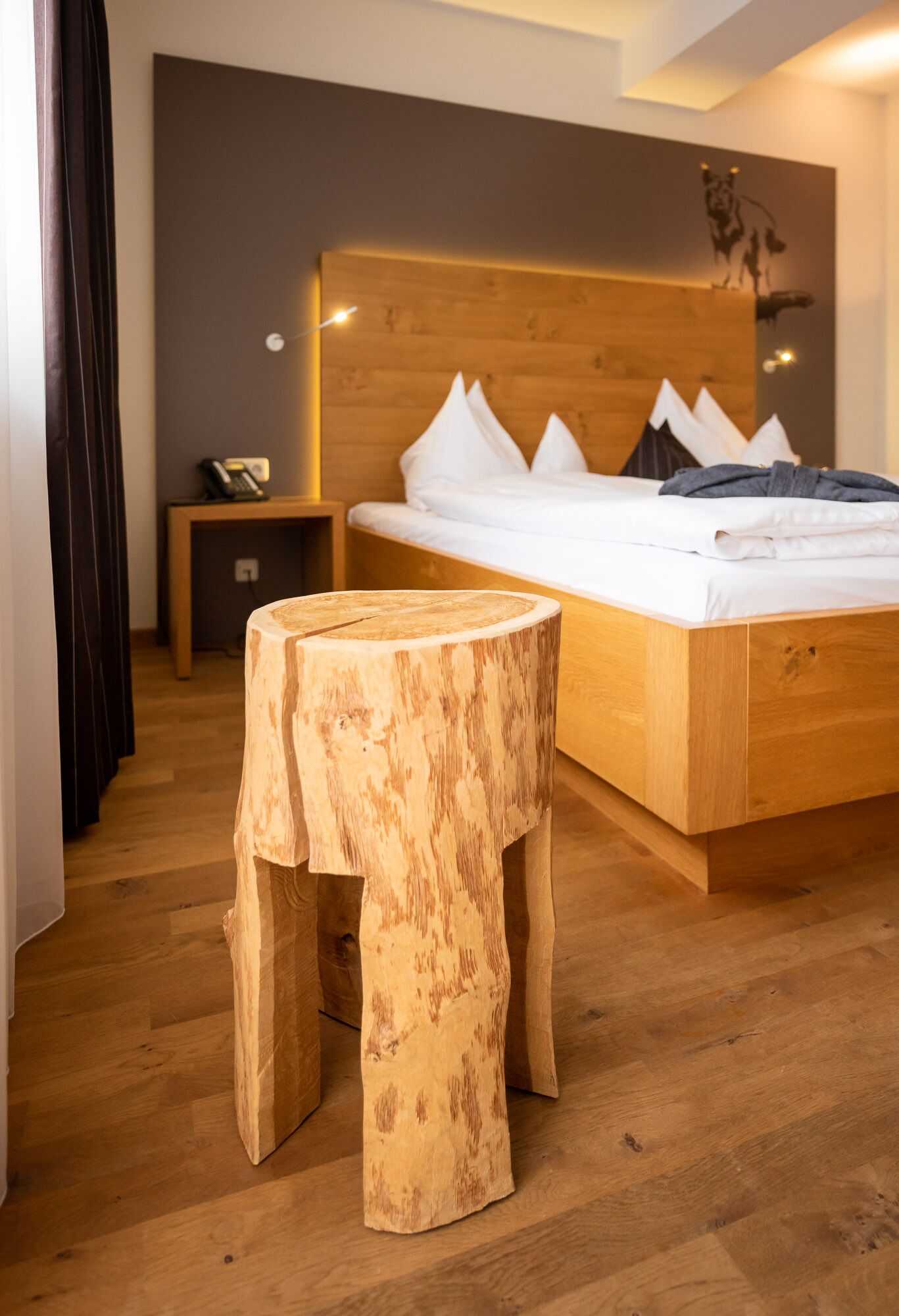 Un dormitorio moderno con estructura de cama de madera, una mesita de noche y un pequeño taburete de madera.
