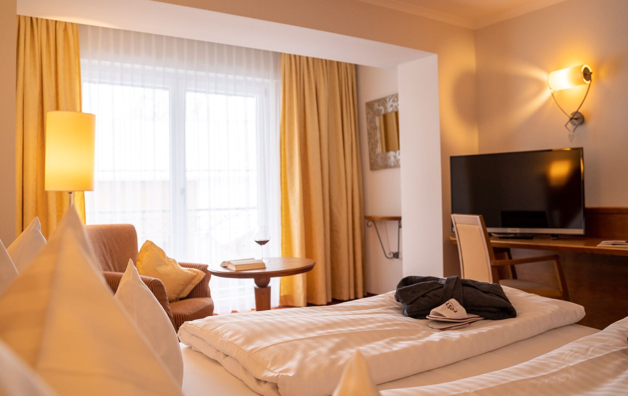 Een hotelkamer met een bed, een televisie, een bureau en een raam met gordijnen.