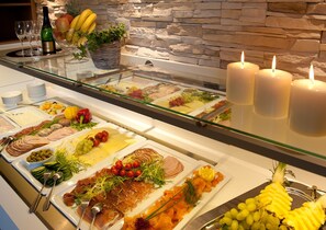 A buffet with various food items, including meats, cheeses, and fruits, with a stone wall and candles in the background. - Landhotel Postwirt (Grafenau)