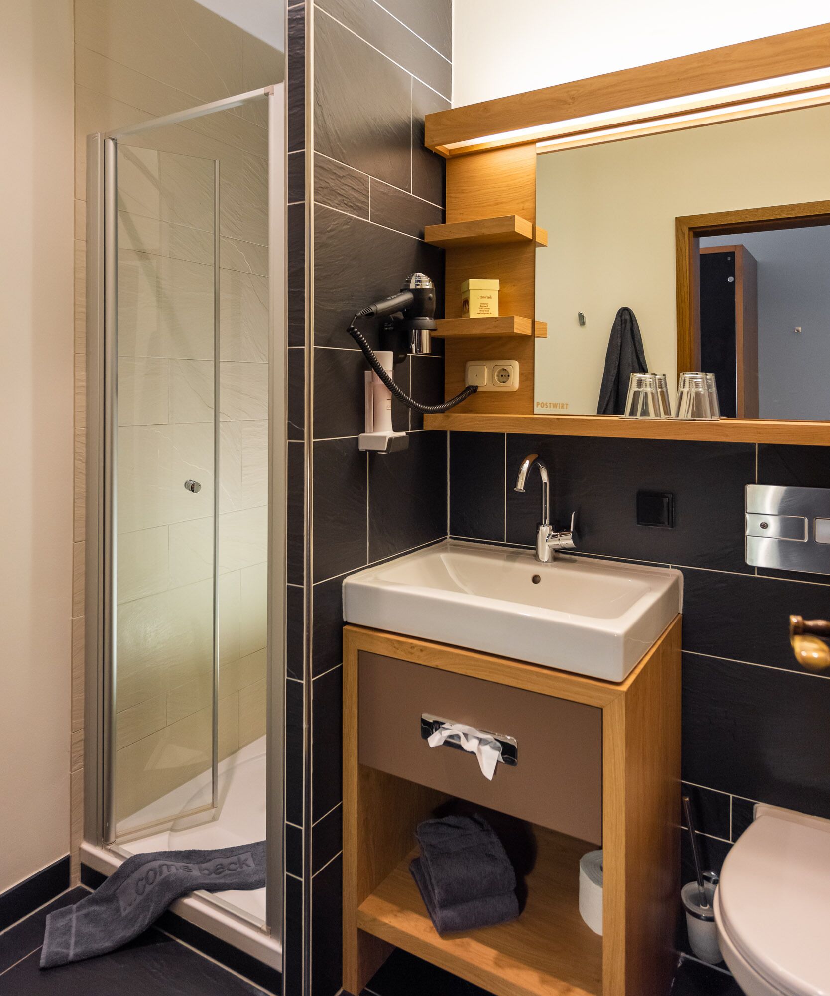 Een moderne badkamer met een douchecabine van glas, een wastafel met een houten meubel en een spiegel erboven.