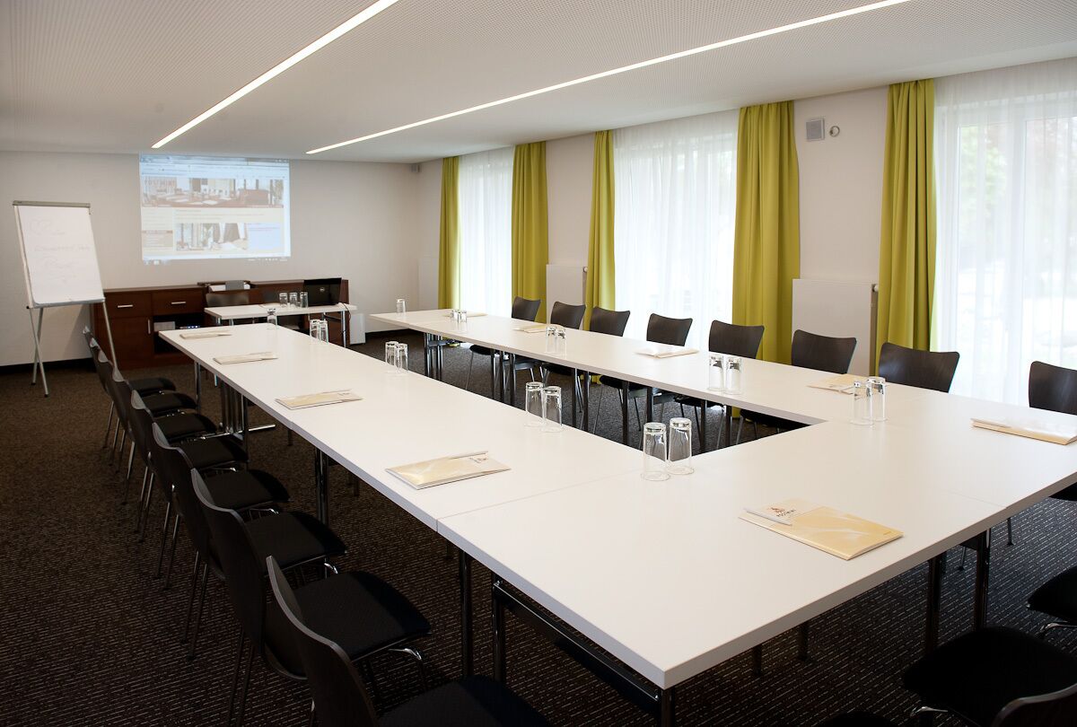 A conference room with a long table, chairs, a whiteboard, and a projection screen.