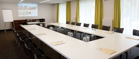 A conference room with a long table, chairs, a whiteboard, and a projection screen.