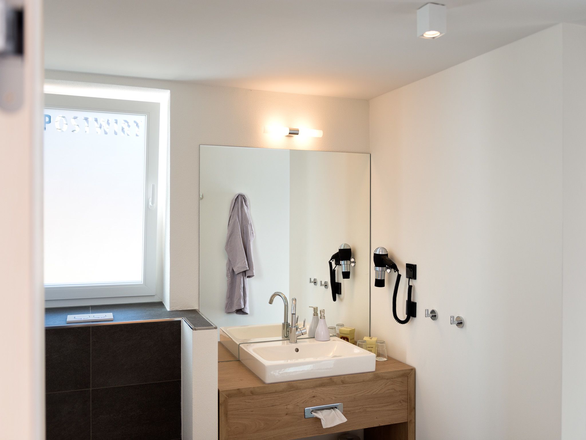 A modern bathroom with a large mirror, a sink, and a hairdryer mounted on the wall.