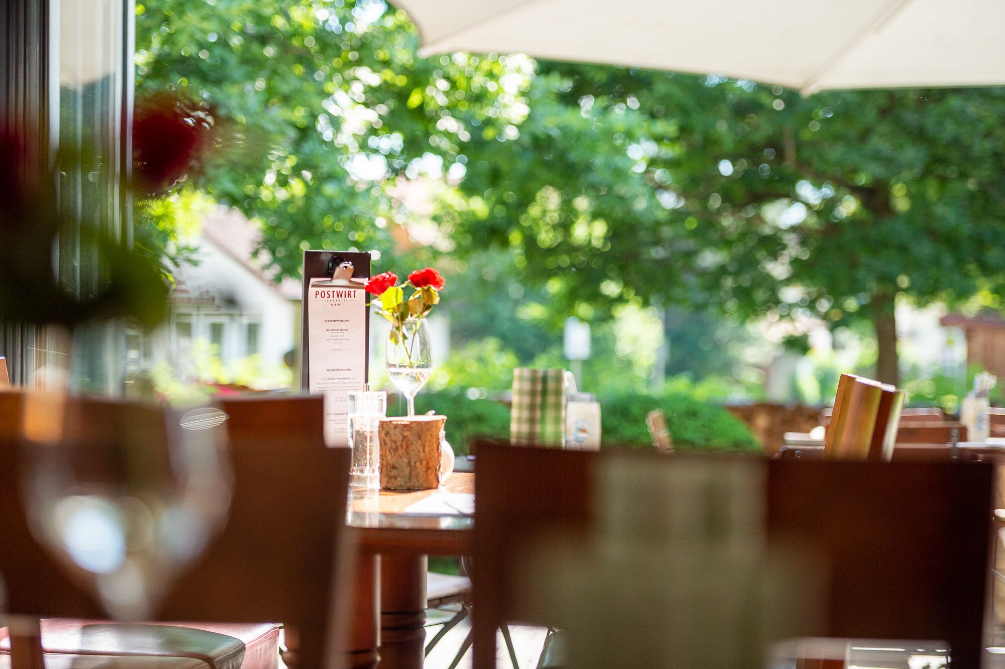Un área de comedor al aire libre con un expositor de menú, un florero con flores y vistas a la vegetación.