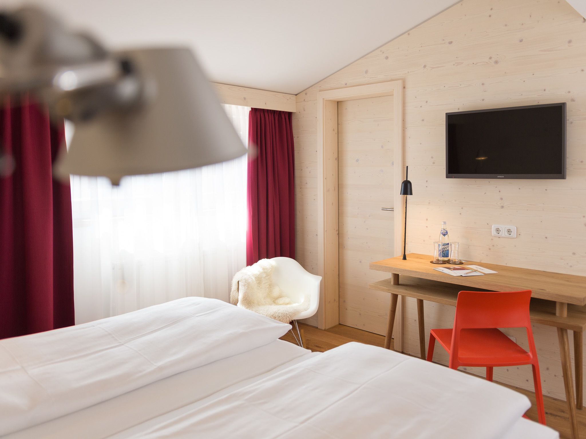 A hotel room with a bed, a desk, a chair, a TV, and a window with curtains.
