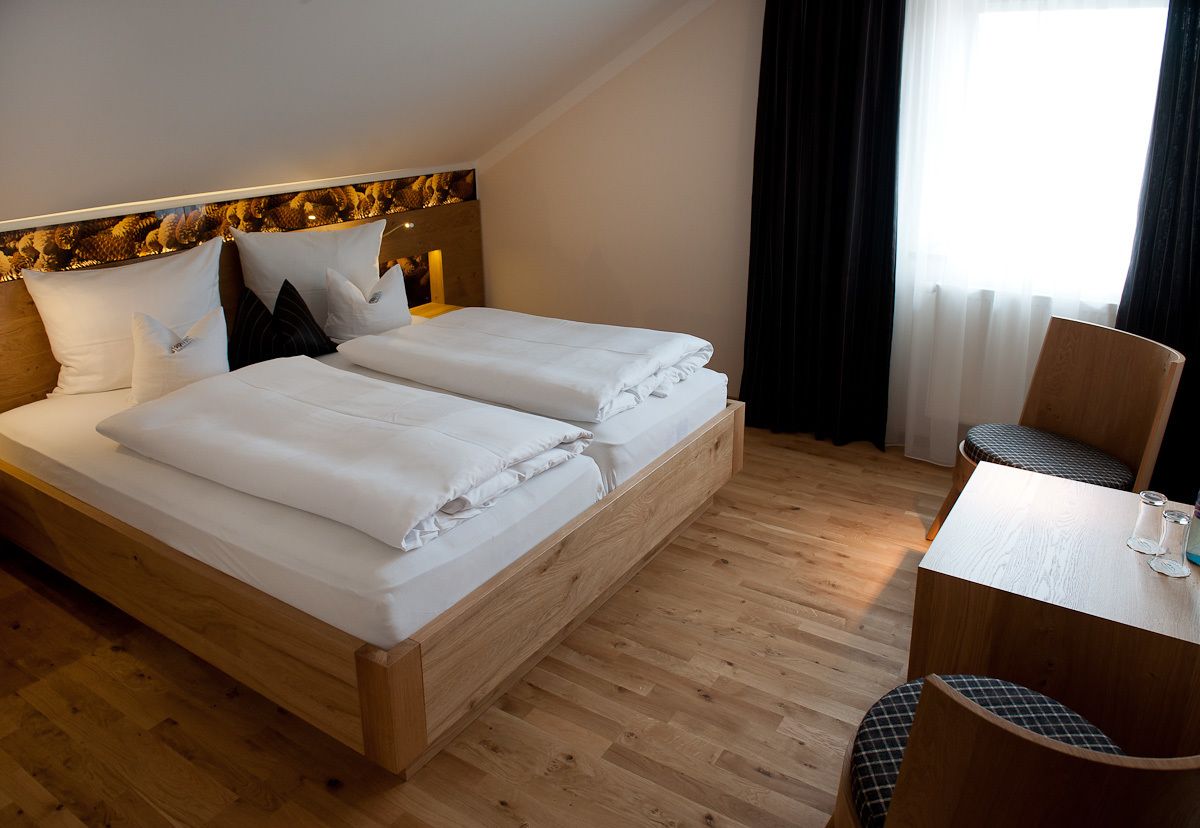A double bed with white linens, a wooden headboard, and a small table with two glasses.
