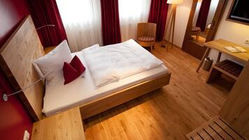 A hotel room with a wooden bed, red curtains, a chair, a desk, and a TV.