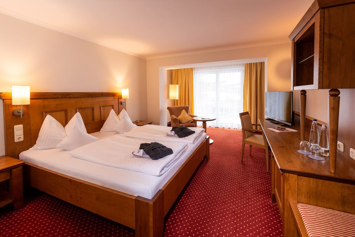 A hotel room with a large bed, two bedside tables, a desk with a chair, a TV, and a window with curtains.
