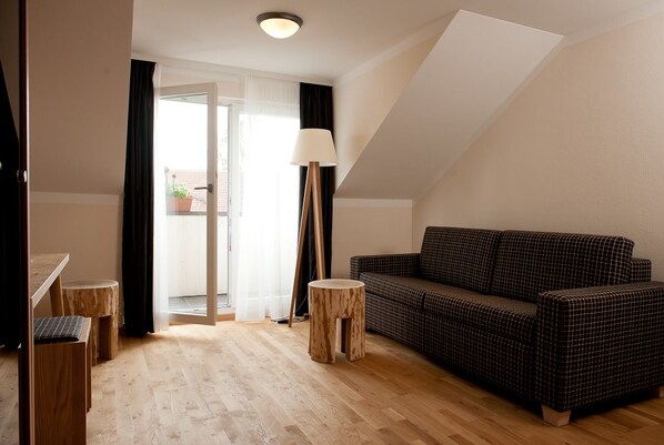 A cozy room with a checkered sofa, a small round table, and a lamp. - Landhotel Postwirt (Grafenau)