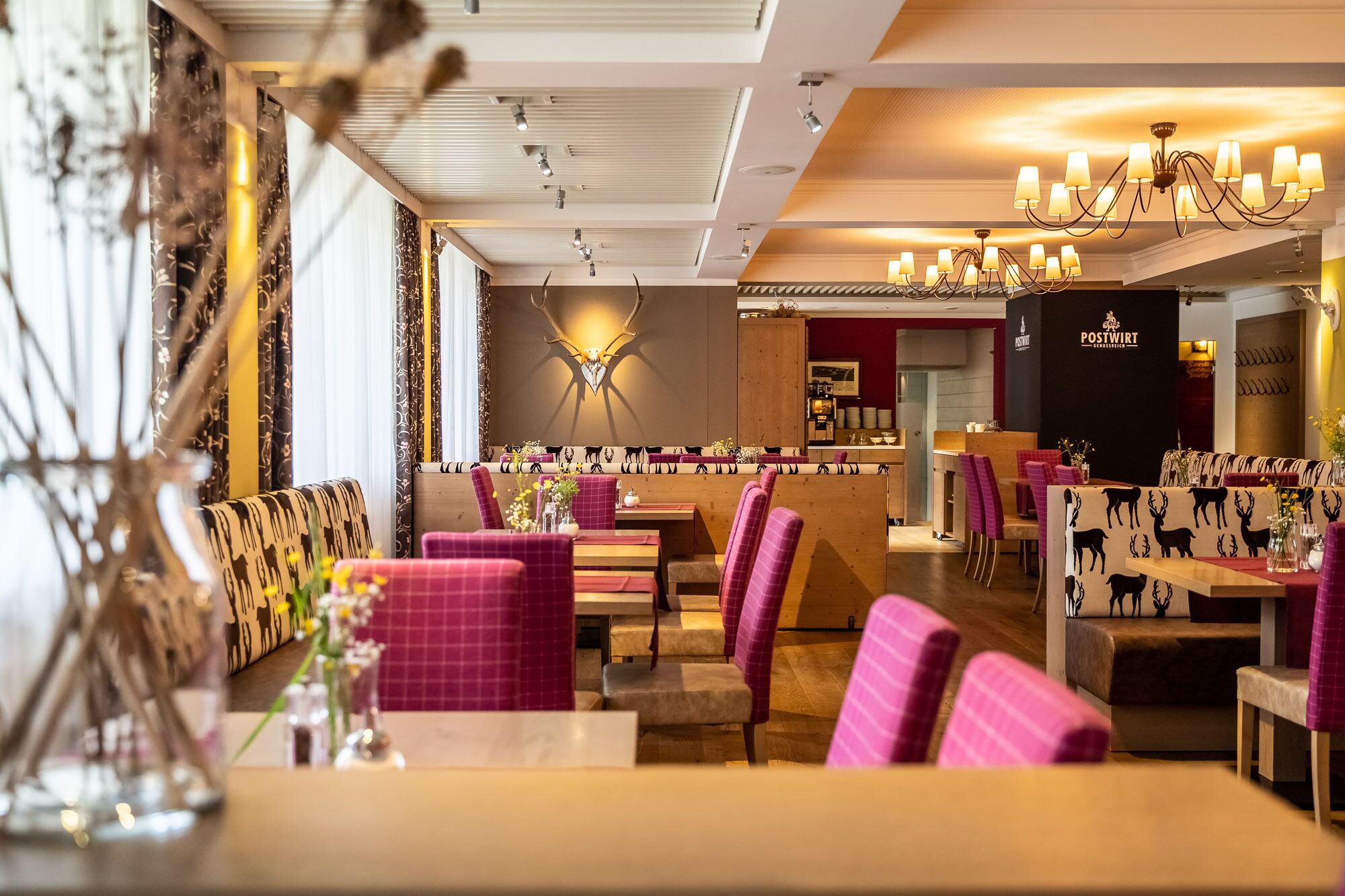 A restaurant with booths and tables, a chandelier, and a wall with a deer pattern.
