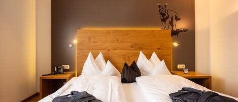 Habitación de hotel con cabecera de madera, ropa de cama blanca, dos mesitas de noche con lámparas, un reloj de pared y la silueta decorativa de un tigre.