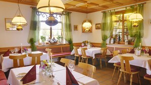 A restaurant with wooden tables and chairs, green curtains, and hanging lamps.