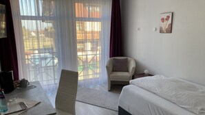 A hotel room with a bed, a chair, a desk with a kettle, and a table.