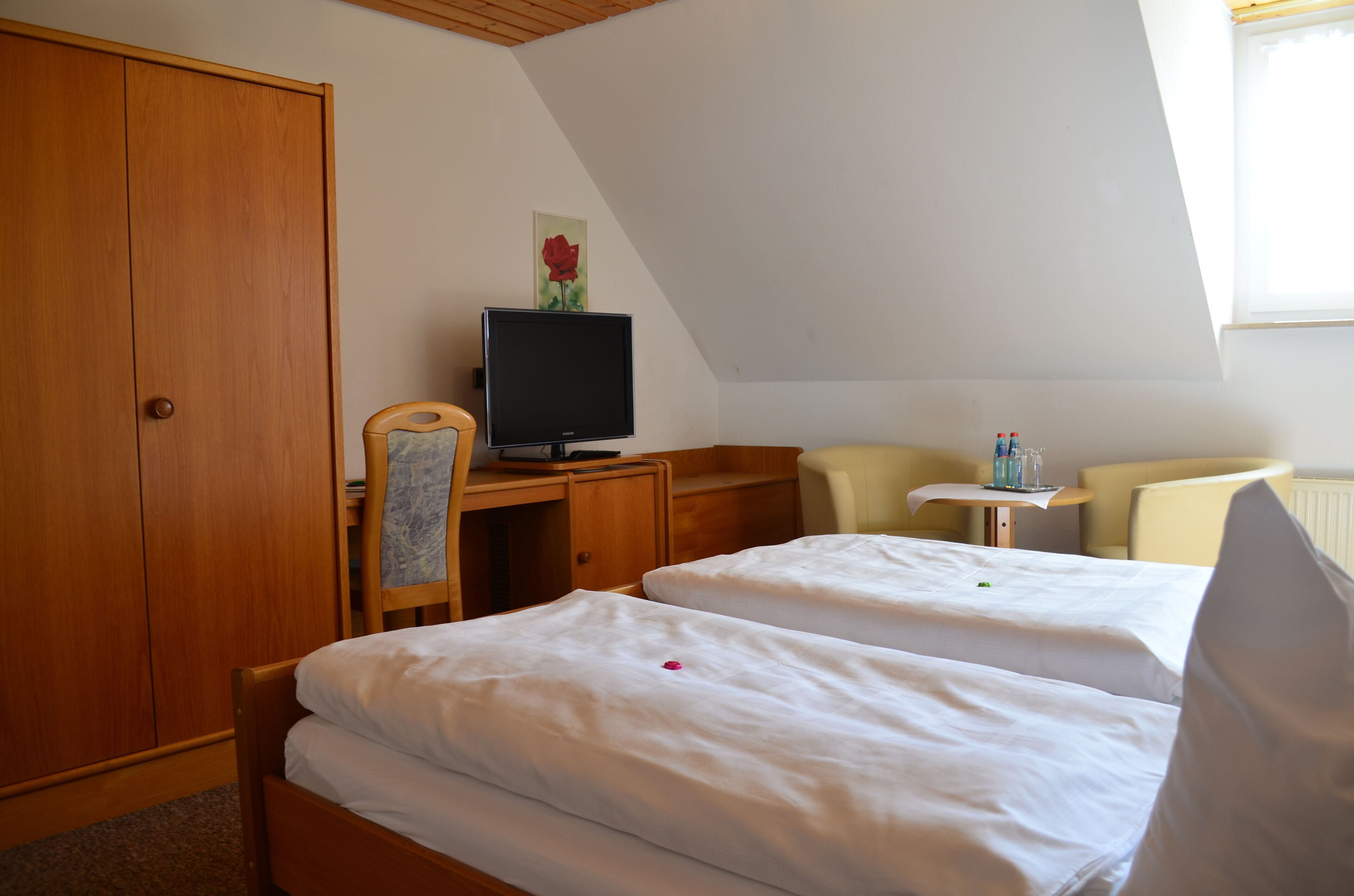 A hotel room with two beds, a desk with a television, a chair, a small table with bottles, and a wardrobe.