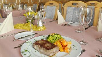 Una mesa de comedor dispuesta con un plato de comida, que incluye un trozo de carne, brócoli y zanahorias, y varias copas de vino.
