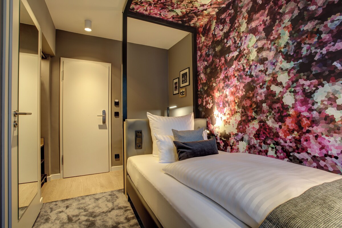Ein Hotelzimmer mit einem Bett, einem Kleiderschrank, einer Tür und einer Wand mit einem Blumenmuster.