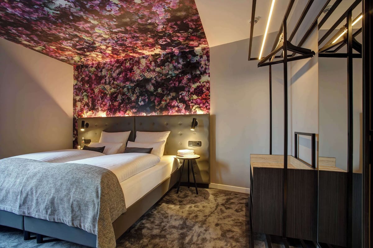 Un dormitorio moderno con una cama grande, cabecera con iluminación integrada, una mesita de noche pequeña y un armario espejo.