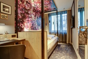 A hotel room with a bed, a desk, a chair, a large floral mural, and a window with curtains. - Vienna House Easy by Wyndham Hamburg City (Hamburg)