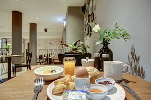 A breakfast table with croissants, eggs, juice, and condiments.