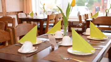 A dining table set with white cups, green napkins, and a vase with a single yellow flower.