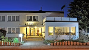 A modern hotel with a name sign, a well-lit entrance, and a brick pathway leading to the door. - Hotel Herrenhof (Lübeck)